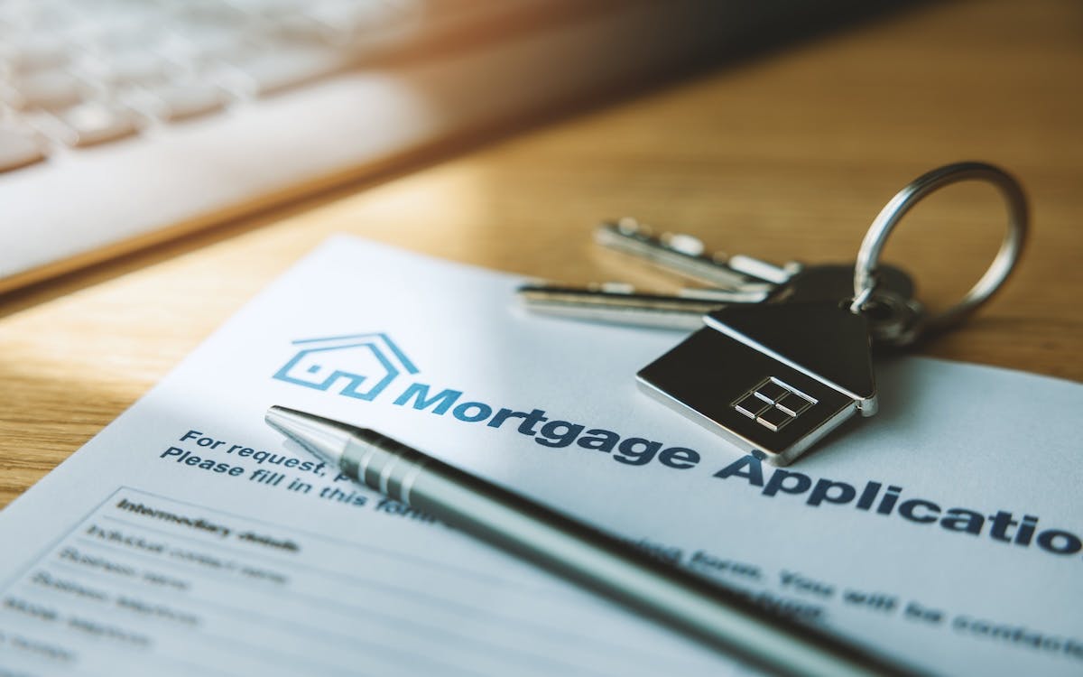 A mortgage application sits on a desk with a pen and a house key on top of it