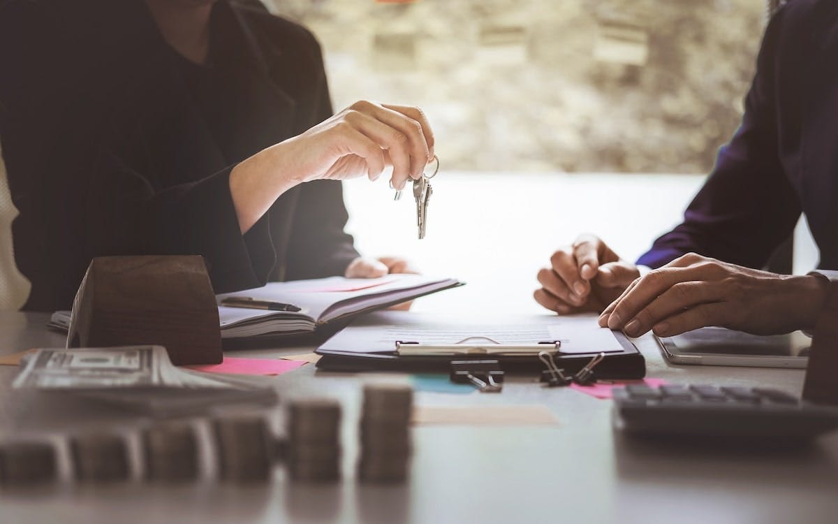 A selling agent hands over the keys to a buyer as they fill out paperwork