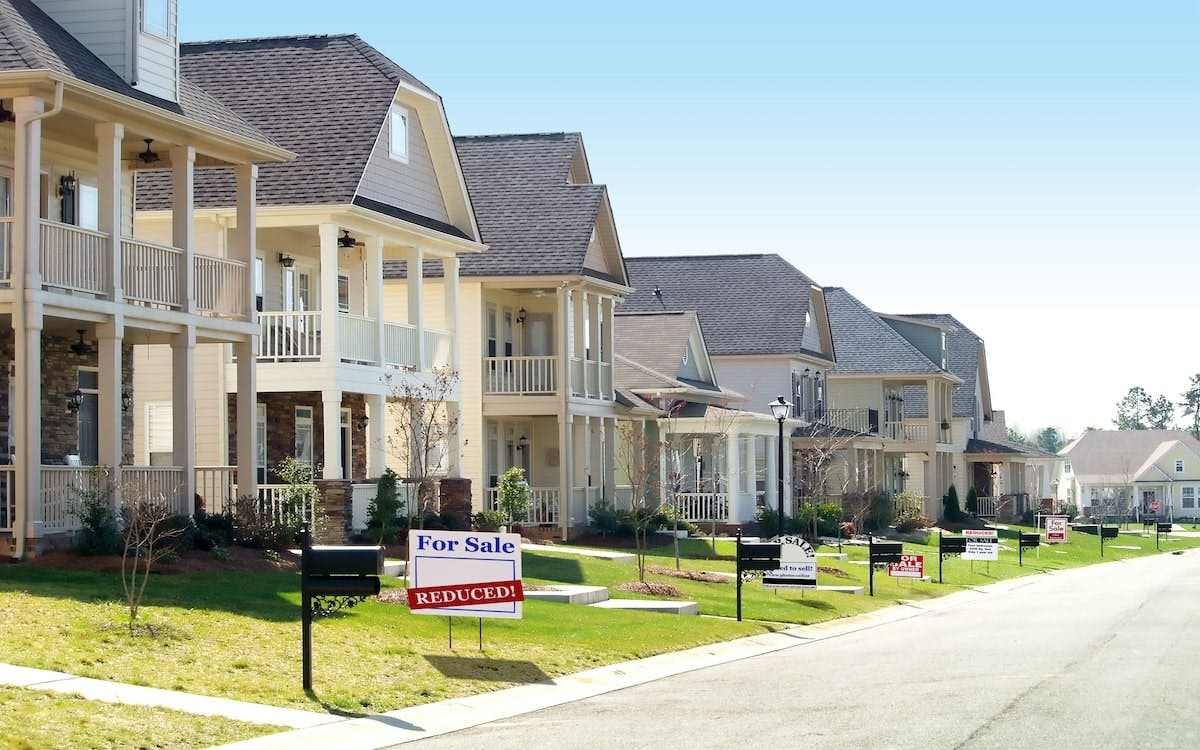 Pictured is a row of homes, and one home has a 'for sale' sign in the front yard with a secondary sign reading 'reduced.'