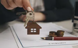 A hand holds up a key above a mortgage loan contract A hand holds up a key above a mortgage loan contract