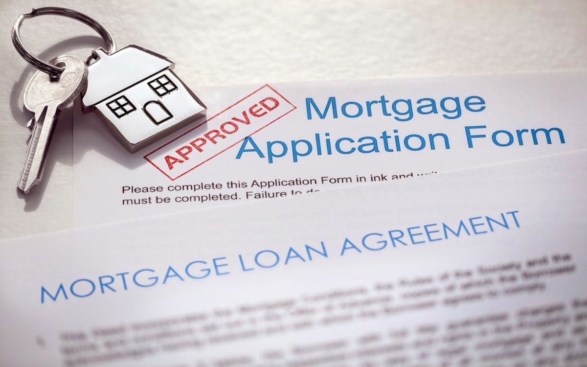 A mortgage loan application with a stamp of approval and a set of house keys on top of it