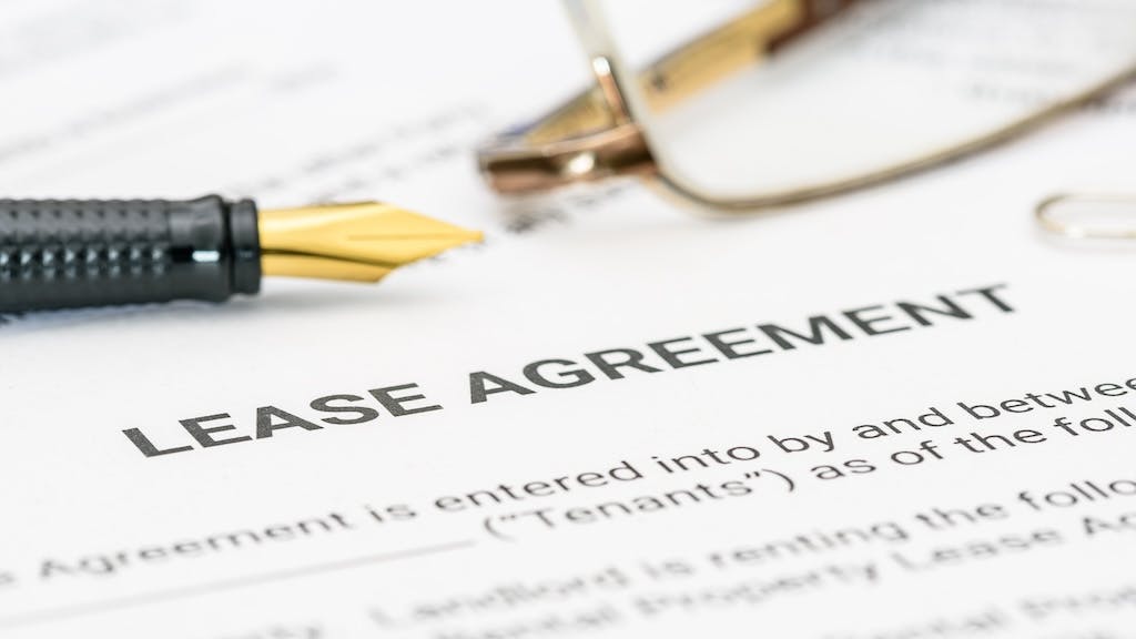 A close-up of a lease agreement with a pair of glasses and a pen sitting on top of them.