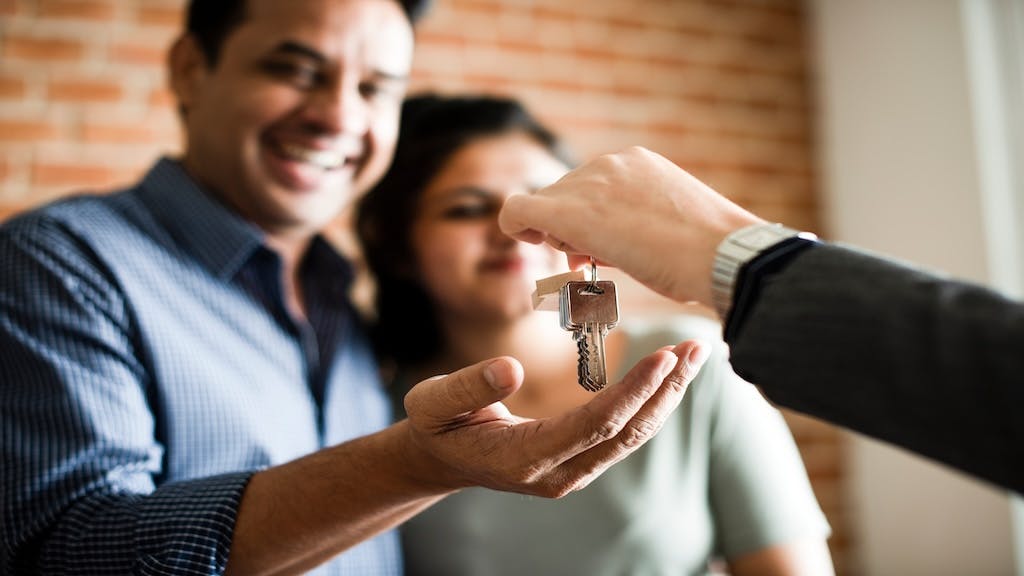 A smiling couple takes house keys from a real estate agent after purchasing their home.