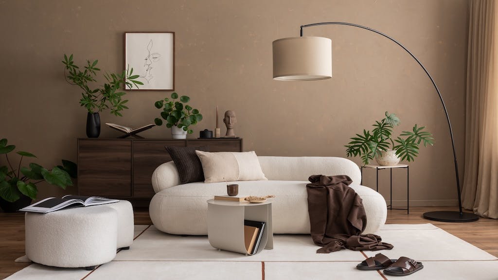 An organic modern living room, with warm brown walls, wooden dresser, large floor lamp, and white couch