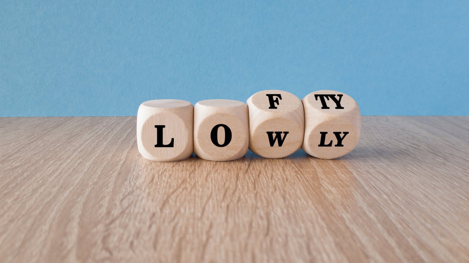 Wooden blocks with 'lowly' letters switching to 'lofty' indicate striving for higher goals.