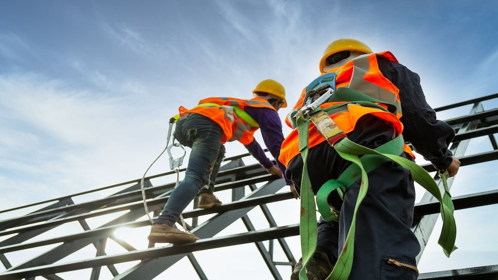 Two construction workers climb up a scaffolding.