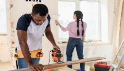 A man in the foreground uses a jig saw while a woman in the background paints the walls of a home they're remodeling to flip.. A man in the foreground uses a jig saw while a woman in the background paints the walls of a home they're remodeling to flip..