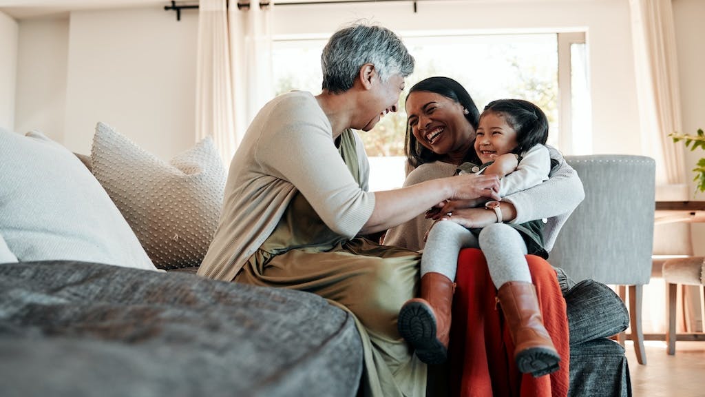 Three generations of women sit in a living room together laughing