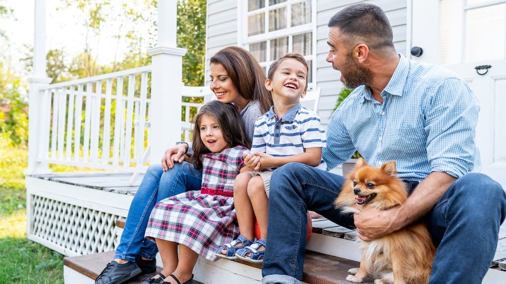 A family sits outside on the front porch of their home