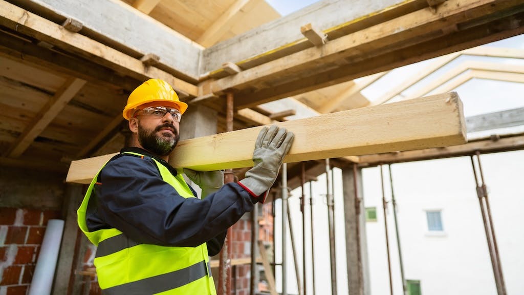 A construction worker carries a beam for a home that is under construction.