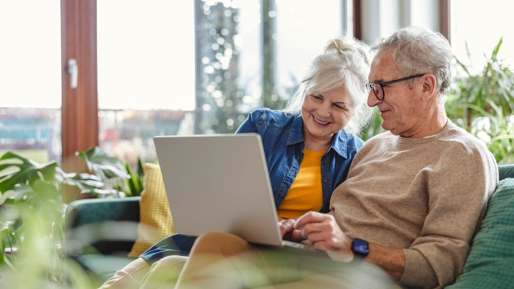 A happy senior couple sits on the couch together in their home