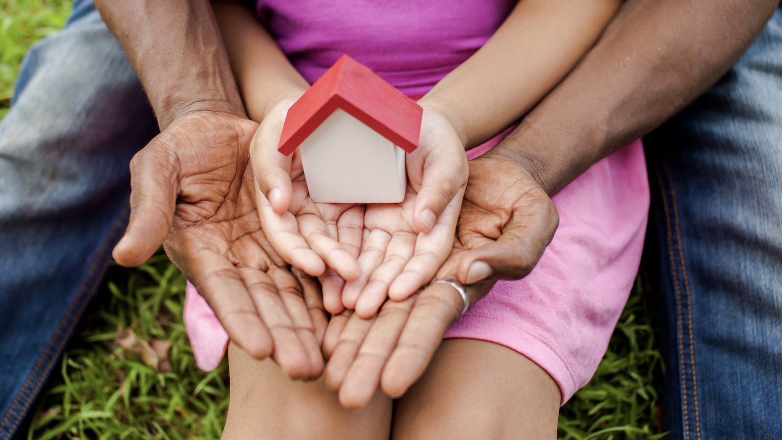 A child's and an adult's hands hold a model house with a red roof to represent fair housing opportunities