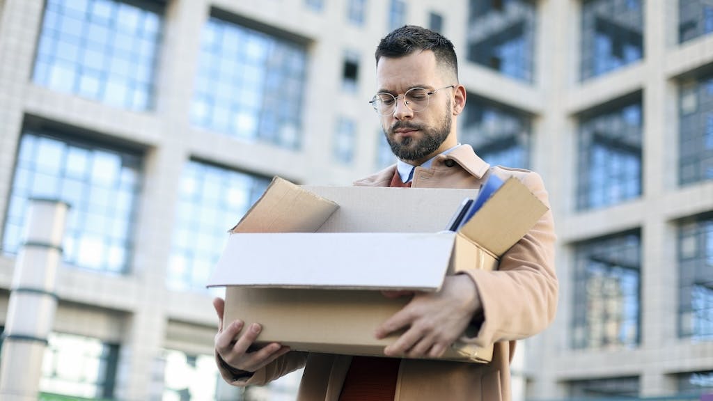 A worker leaves his employment in an office building with a box in hand, representing the layoffs of federal workers by the Trump administration