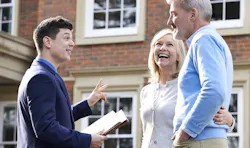 A salesperson meeting with prospective homebuyers in front of a brick house. A salesperson meeting with prospective homebuyers in front of a brick house.