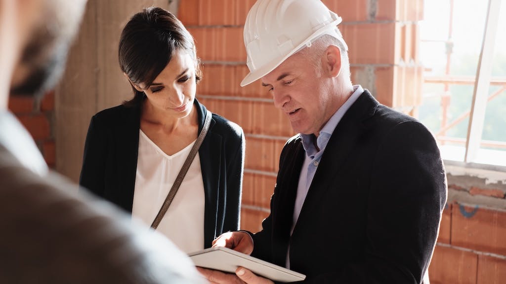 Home builder wearing a hard hat speaks with clients on the jobsite.