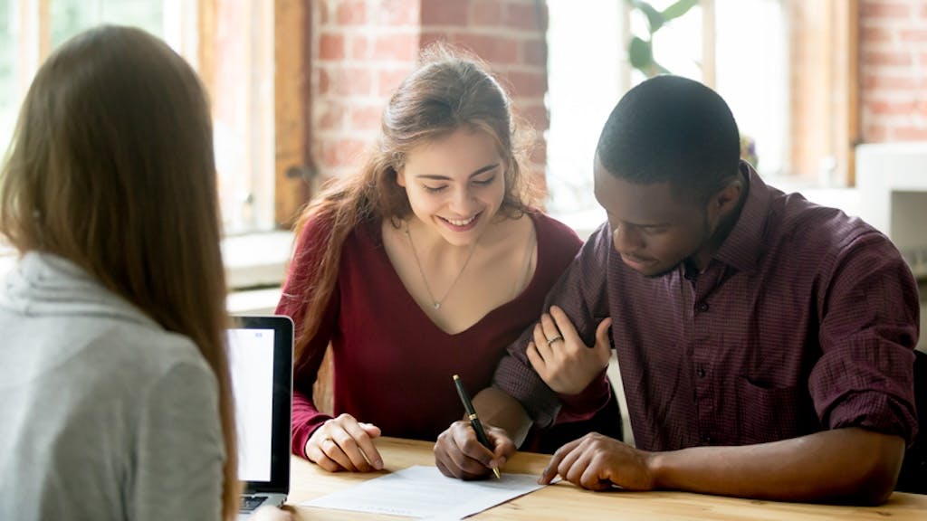 In the process of buying a new home, a couple signs documents excitedly with a real estate agent