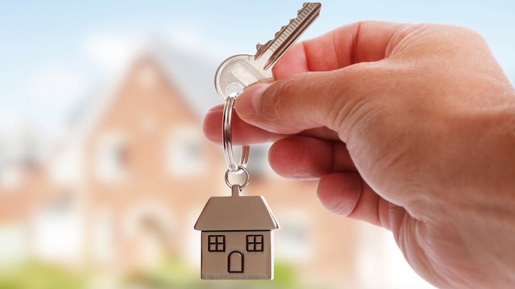 Foreign homebuyer holds up house key with home in background