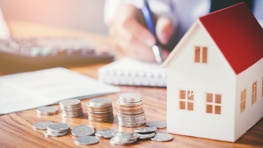 Model home next to stack of coins, indicating housing costs