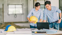 A man and a woman holding a hard hat looks over plans on a laptop at a construction site A man and a woman holding a hard hat looks over plans on a laptop at a construction site