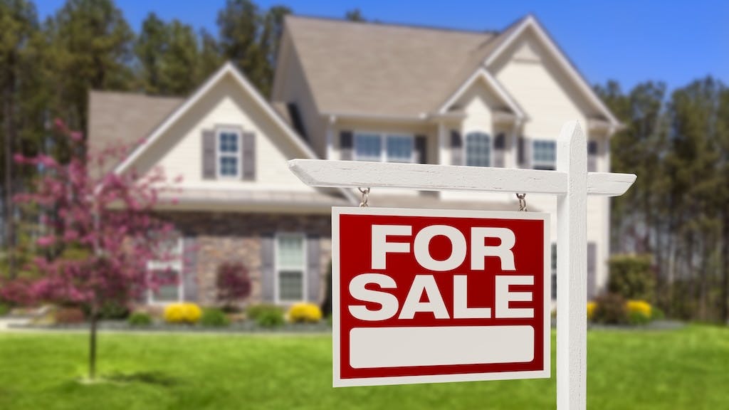 A red 'For Sale' sign in the front yard of a home