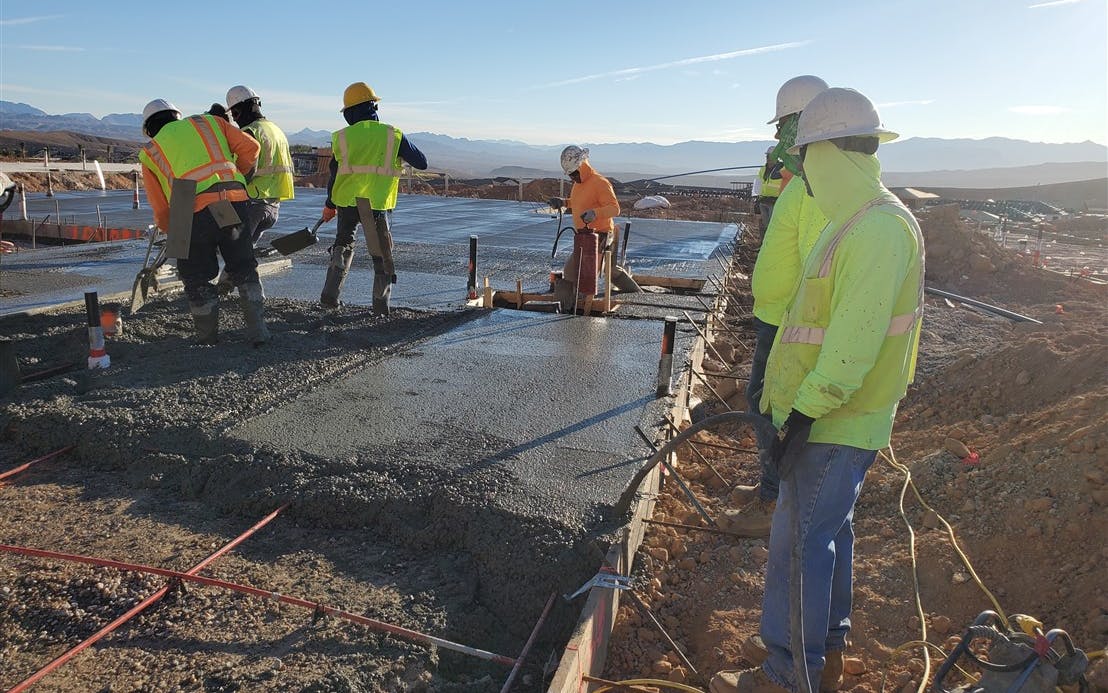 A concrete foundation and slab being properly consolidated by means of vibration, with an adequate number of workers on site to place and finish the pour.