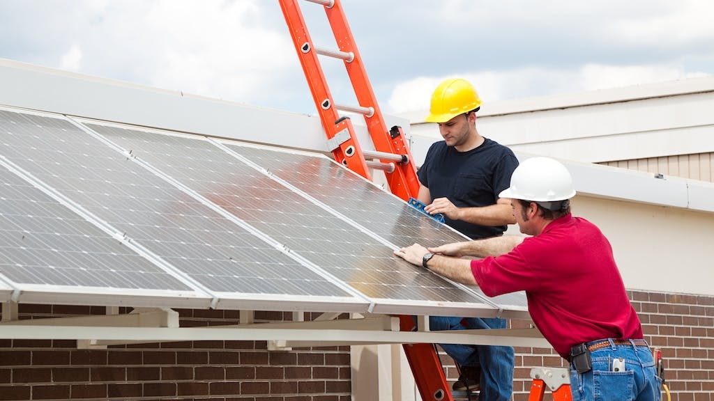 Workers install solar panels onto the roof of a home