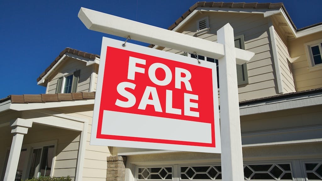 For sale sign posted in the front yard of a single-family home