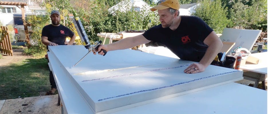Adhesive Seals The Panels To The Framing After Snapping Lines Indicating Framing Members, The Crew Applies Foam Subfloor Adhesive To Assure A Solid Bond While Waiting For Closed Cell Spray Foam To Be Added To Joist Cavities From Above