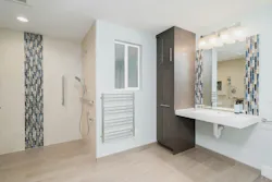 In this remodel, which won Gold in the NAHB’s BALA Awards program, Irons Brothers Construction transformed a rec room and existing powder room into a barrier-free space to accommodate a client who unexpectedly became disabled. The design focused on creating an open, functional layout that accommodated medical equipment and a large power wheelchair. Key features include a ceiling-mounted Hoyer lift, spacious bedroom with multiple layout options, and a fully accessible bathroom with a curb-less shower, floating sink counter, side-mounted faucet, and tall pullout cabinet for easy access to toiletries. The toilet has a washlet feature, which Irons says he installs in about 75% of his projects—for clients young and old, able bodied or otherwise. The suite's entry was designed to allow for future ramp installation, while widened doorways and motion-sensor door openers improve accessibility. In this remodel, which won Gold in the NAHB’s BALA Awards program, Irons Brothers Construction transformed a rec room and existing powder room into a barrier-free space to accommodate a client who unexpectedly became disabled. The design focused on creating an open, functional layout that accommodated medical equipment and a large power wheelchair. Key features include a ceiling-mounted Hoyer lift, spacious bedroom with multiple layout options, and a fully accessible bathroom with a curb-less shower, floating sink counter, side-mounted faucet, and tall pullout cabinet for easy access to toiletries. The toilet has a washlet feature, which Irons says he installs in about 75% of his projects—for clients young and old, able bodied or otherwise. The suite's entry was designed to allow for future ramp installation, while widened doorways and motion-sensor door openers improve accessibility.