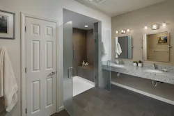 This primary bathroom was remodeled for a future wheelchair user. The reworked space includes a curbless shower that’s large enough to accommodate a caregiver if needed, a floating stone countertop, and mirrors that tilt toward a seated user. Grab bars were added throughout the space, and lighting was upgraded. A new storage closet features a jamb switch that automatically turns on the lights when the door opens. This primary bathroom was remodeled for a future wheelchair user. The reworked space includes a curbless shower that’s large enough to accommodate a caregiver if needed, a floating stone countertop, and mirrors that tilt toward a seated user. Grab bars were added throughout the space, and lighting was upgraded. A new storage closet features a jamb switch that automatically turns on the lights when the door opens.
