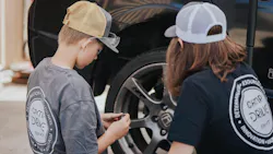 A youth looks over a car with a technician. A youth looks over a car with a technician.