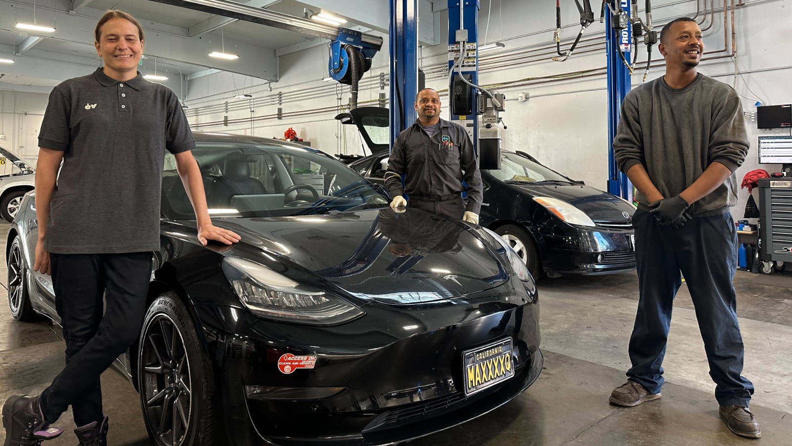 A decade of development: Earthling technicians Cara, Jeo, and Leon with a Tesla Model 3 and a Gen 2 Prius.