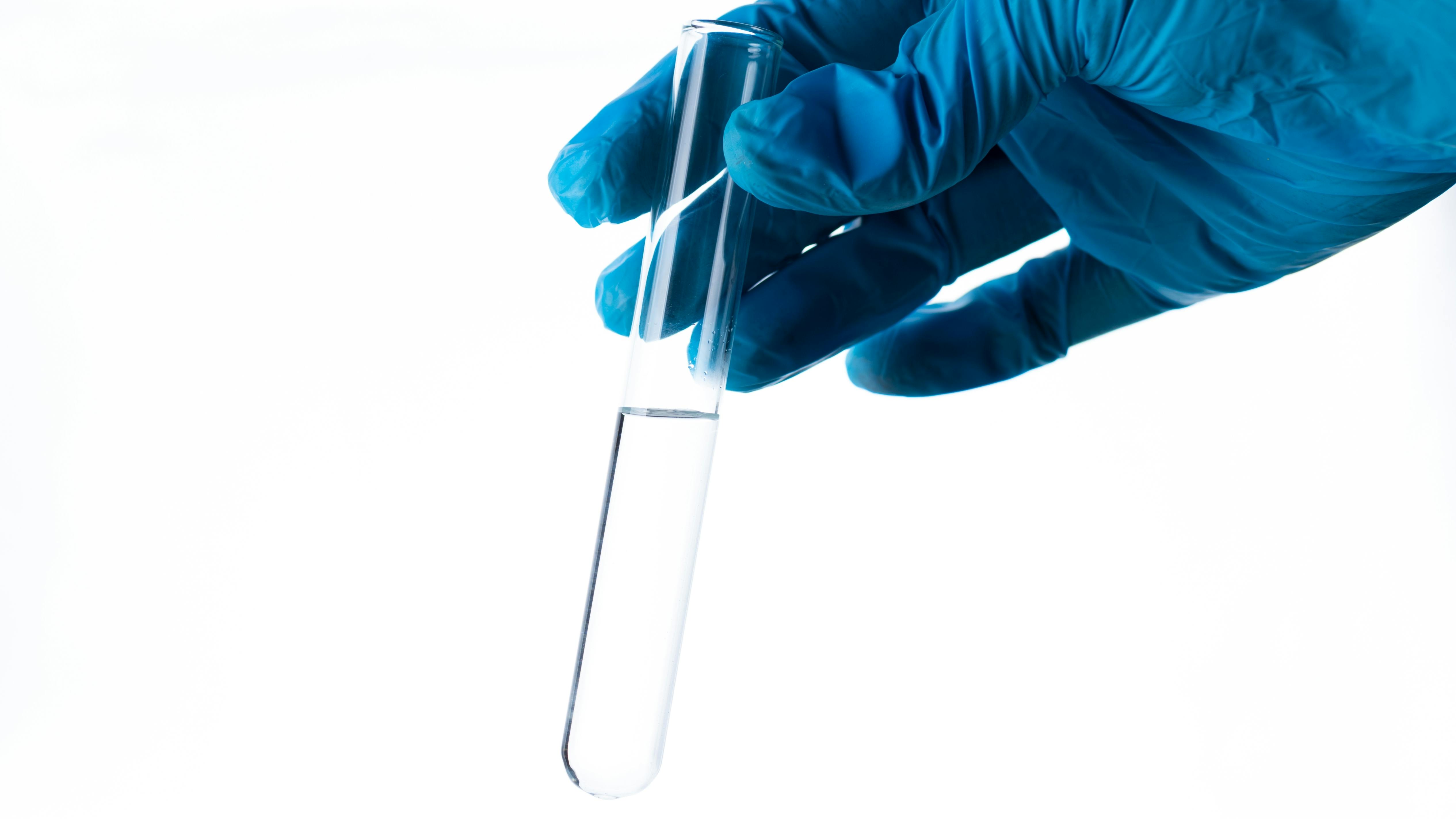 A gloved hand holding a test tube of water
