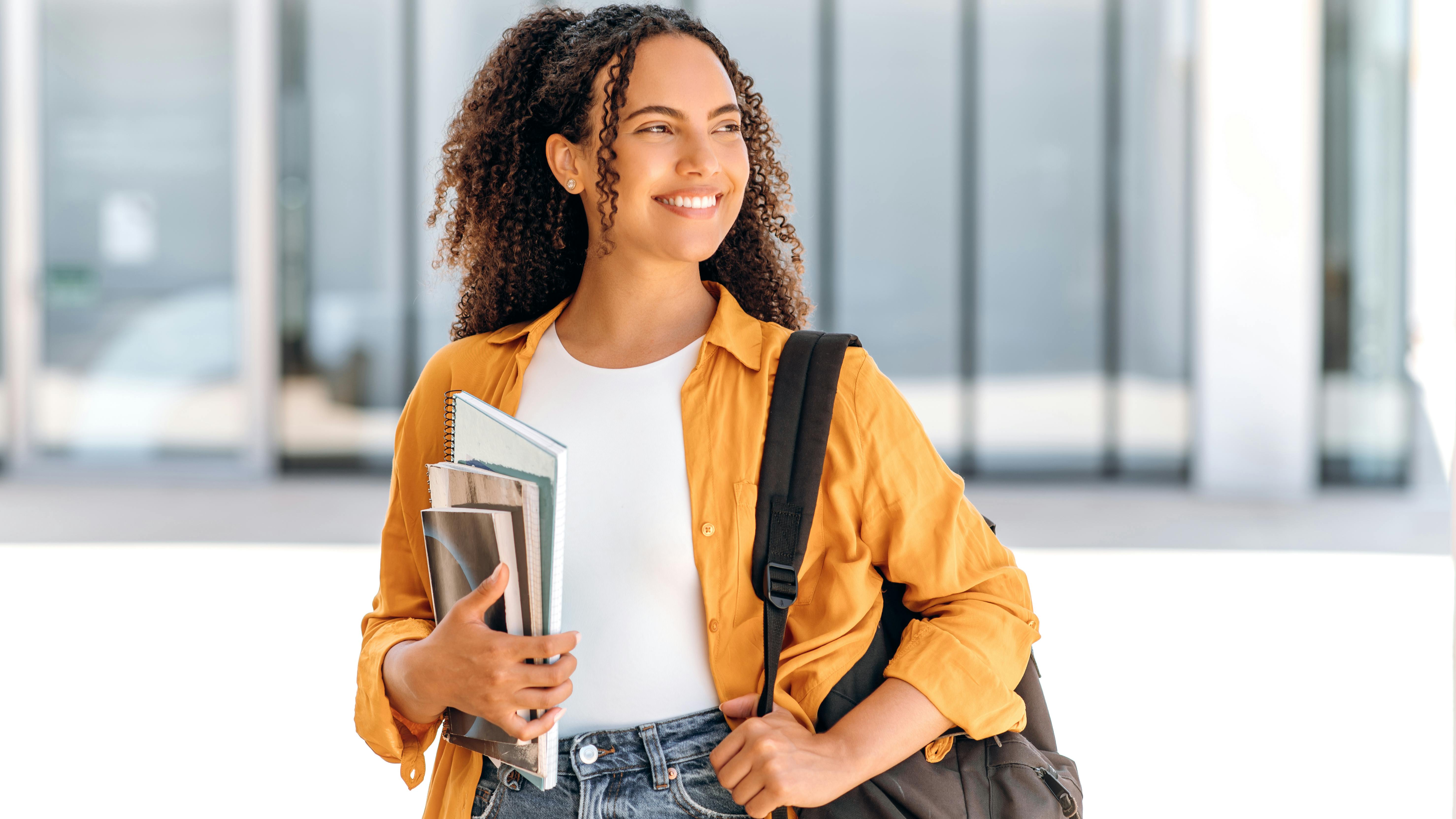 smiling woman holding books and a backpack