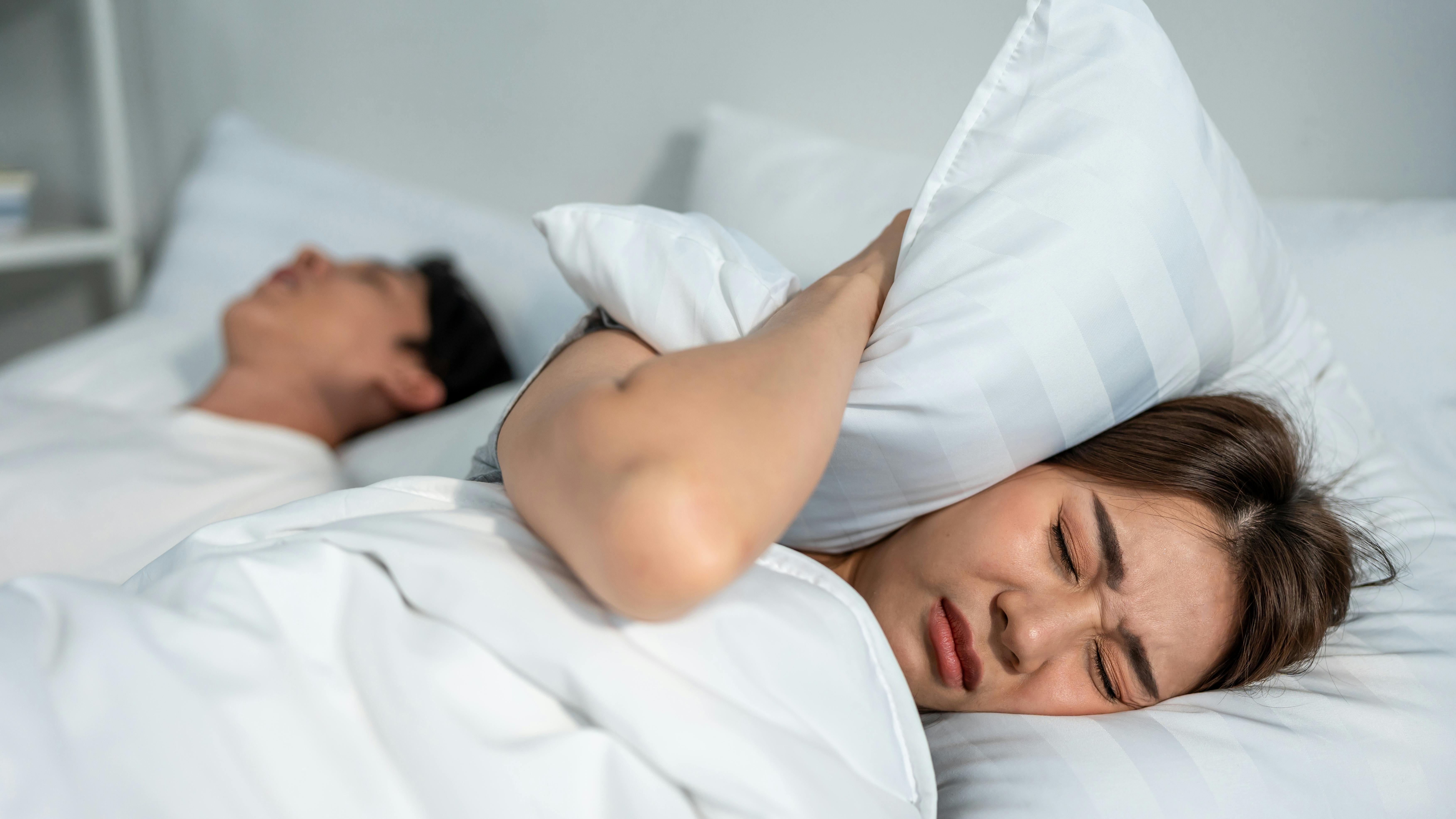 woman covering her ear with a pillow to drown out the snoring of her partner