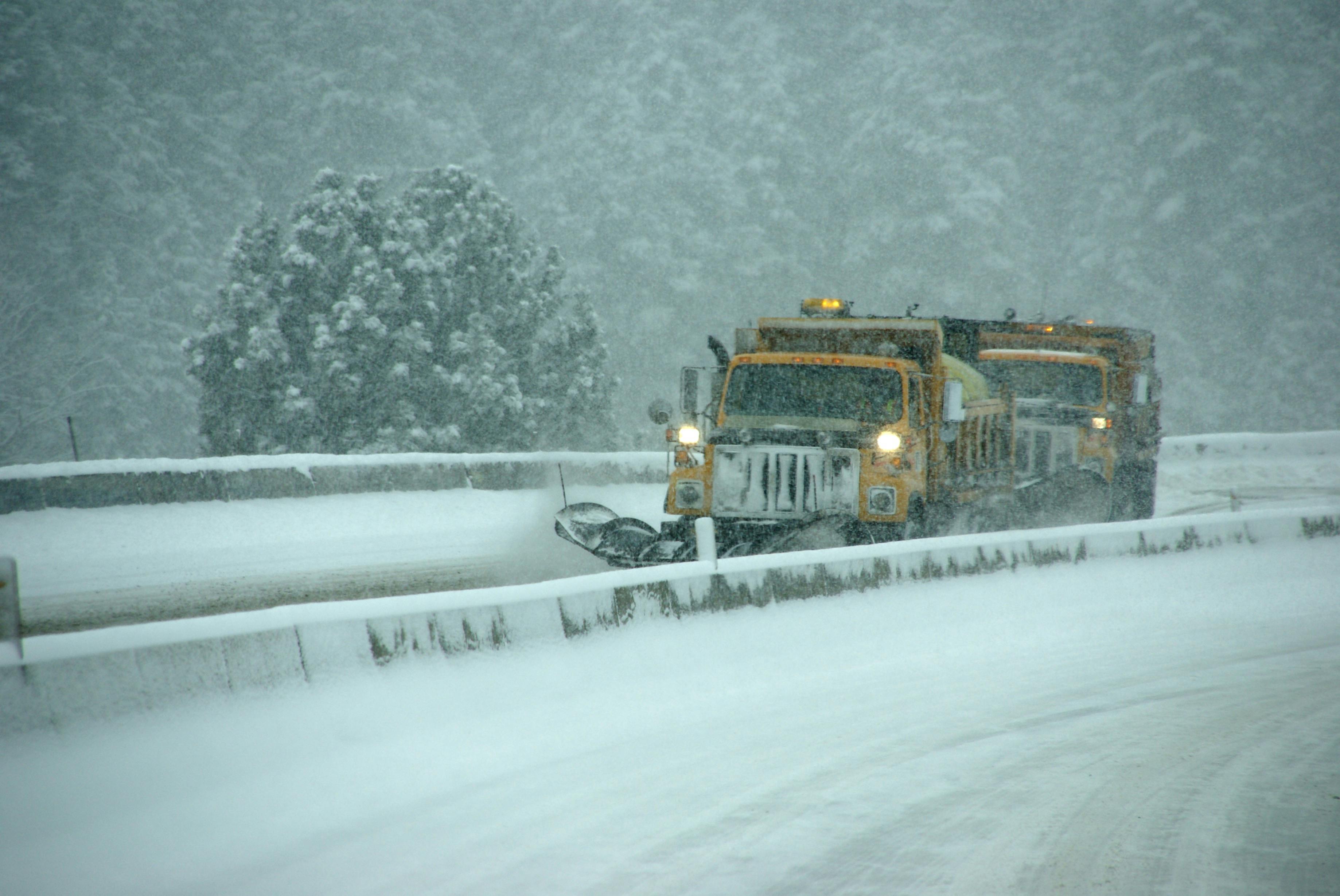 A snow plow clearing a roadway blanketed with heavy snow.