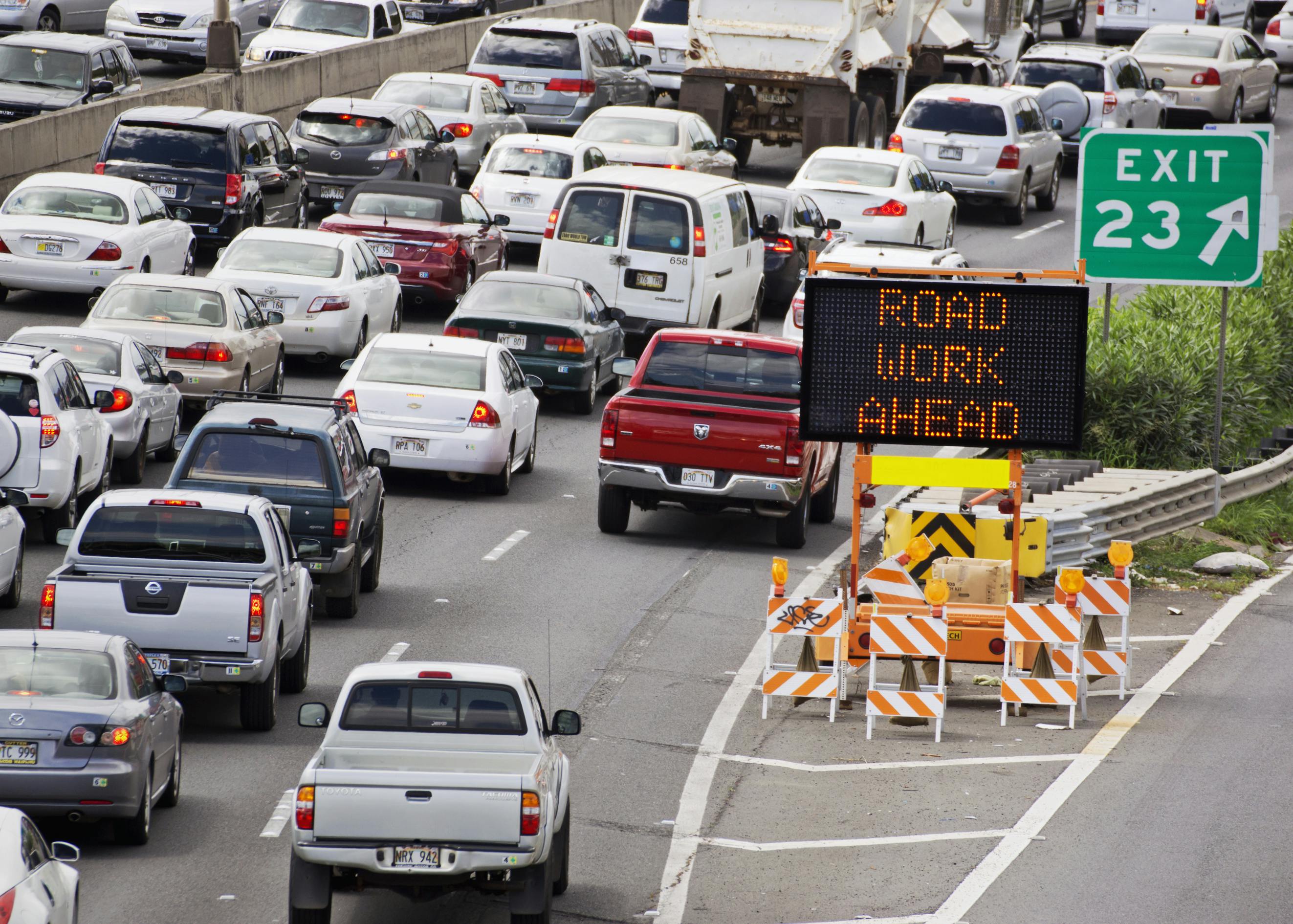 Bumper to bumper traffic on a highway with a sign informing drivers of an upcoming work zone ahead.