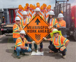 Road workers gathered around an orange construction sign stating 'Meaningful Work Ahead.' Road workers gathered around an orange construction sign stating 'Meaningful Work Ahead.'