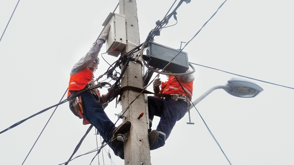 A crew installs a concentrator on a concrete pole