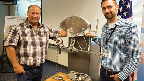 Rocky Mountain foreman III lineman Ron Burbridge and headquarters civil engineer Cody Neyens with the Burbolifter a device developed and fabricated by Burbridge that allows crews to lift optical ground wire without the use of a jib crane Now crews can use a helicopter for optical ground wire hardware replacement instead of a bucket truck and increase productivity by 500
