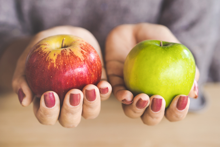 A pair of hands holding a green and a red apple