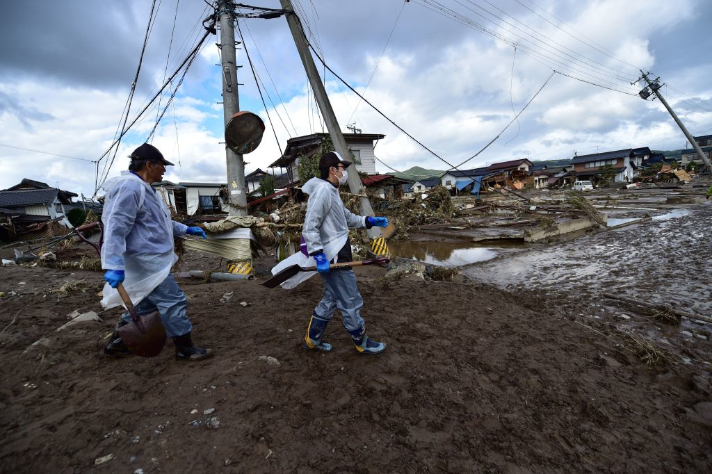 Workers walk past damaged homes and debris
