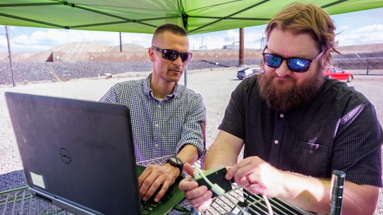 Sandia National Laboratories cybersecurity expert Adrian Chavez, left, and computer scientist Logan Blakely work to integrate a single-board computer with their neural-network AI into the Public Service Company of New Mexico&rsquo;s test site. This code monitors the grid for cyberattacks and physical issues.