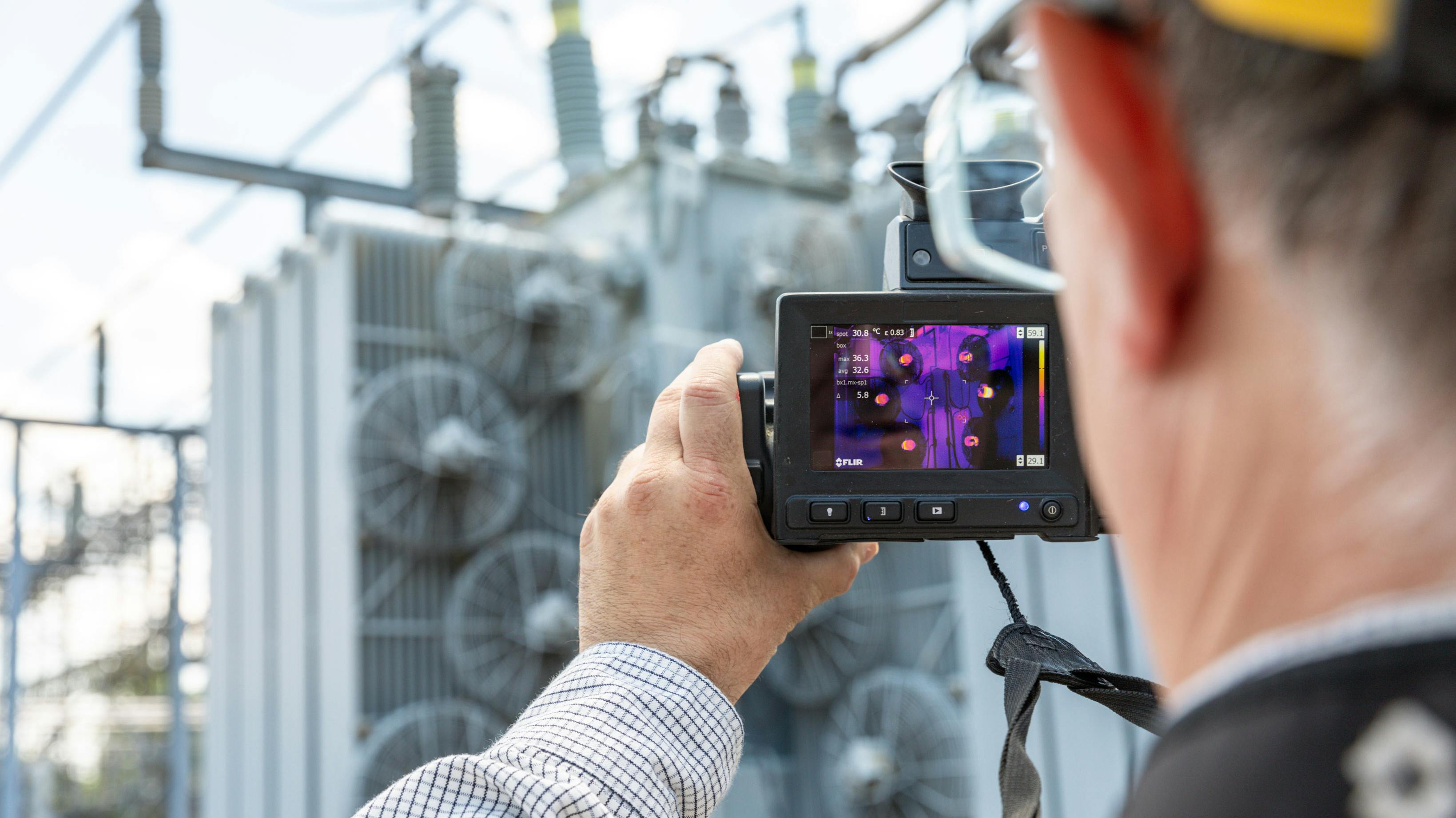 A worker uses an infrared camera to capture imagery of a transformer cooling fan bank. The photo is part of the eBook materials used to train workers on infrared inspection and leak detection.