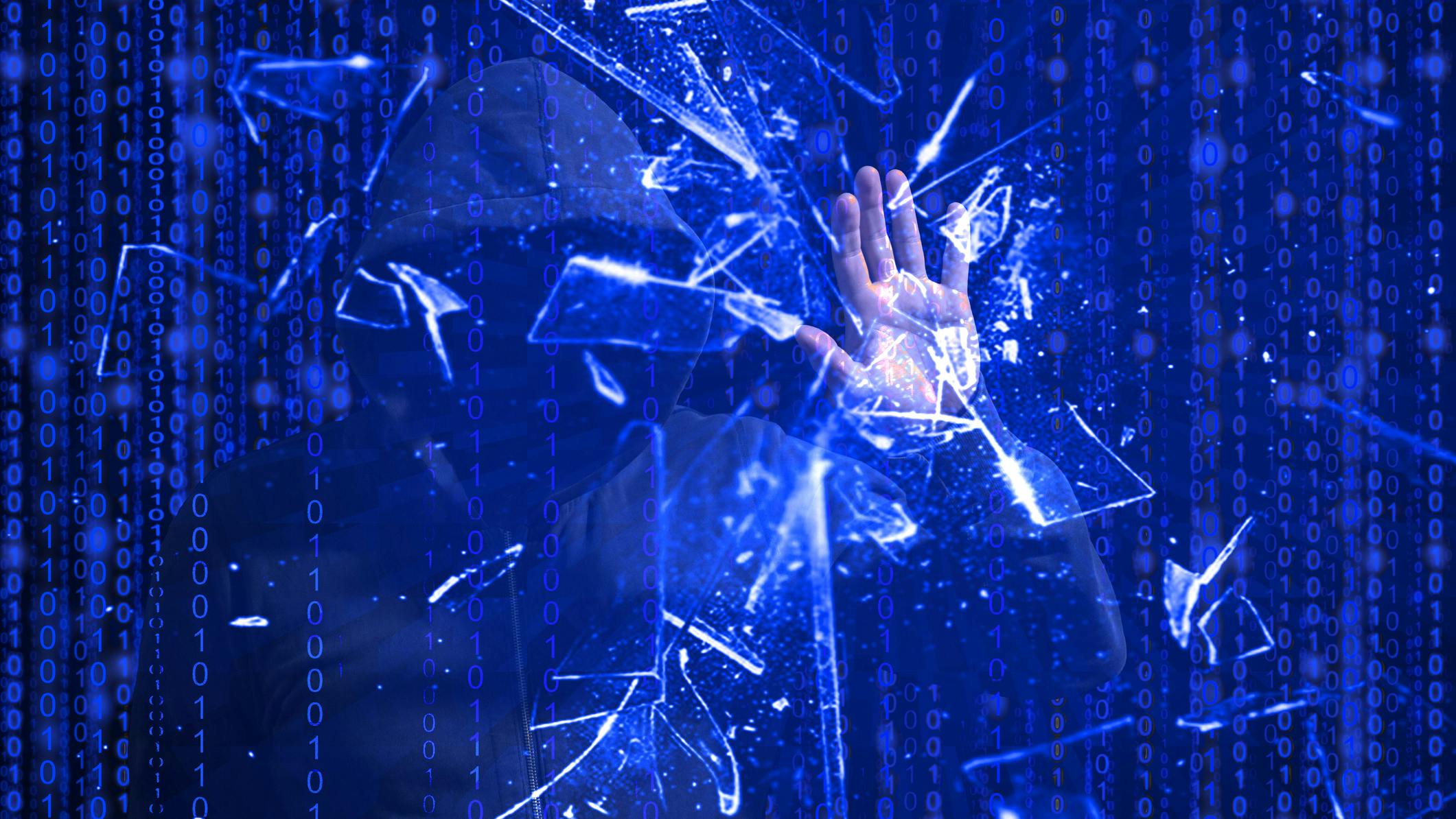 Hooded hacker smashing blue screen with one hand.in front of blue binary background representing cybersecurity.
