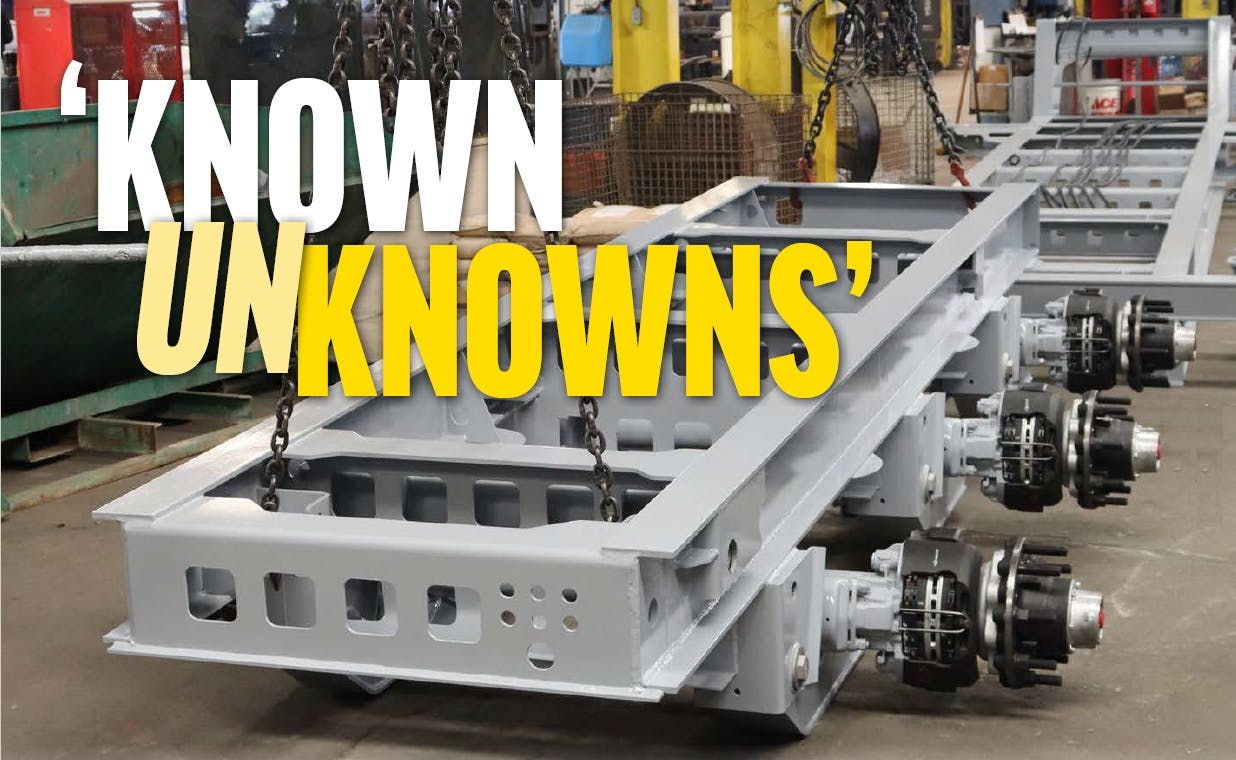 Newly painted trailer frame going through assembly line suspended above shop floor by heavy chains.