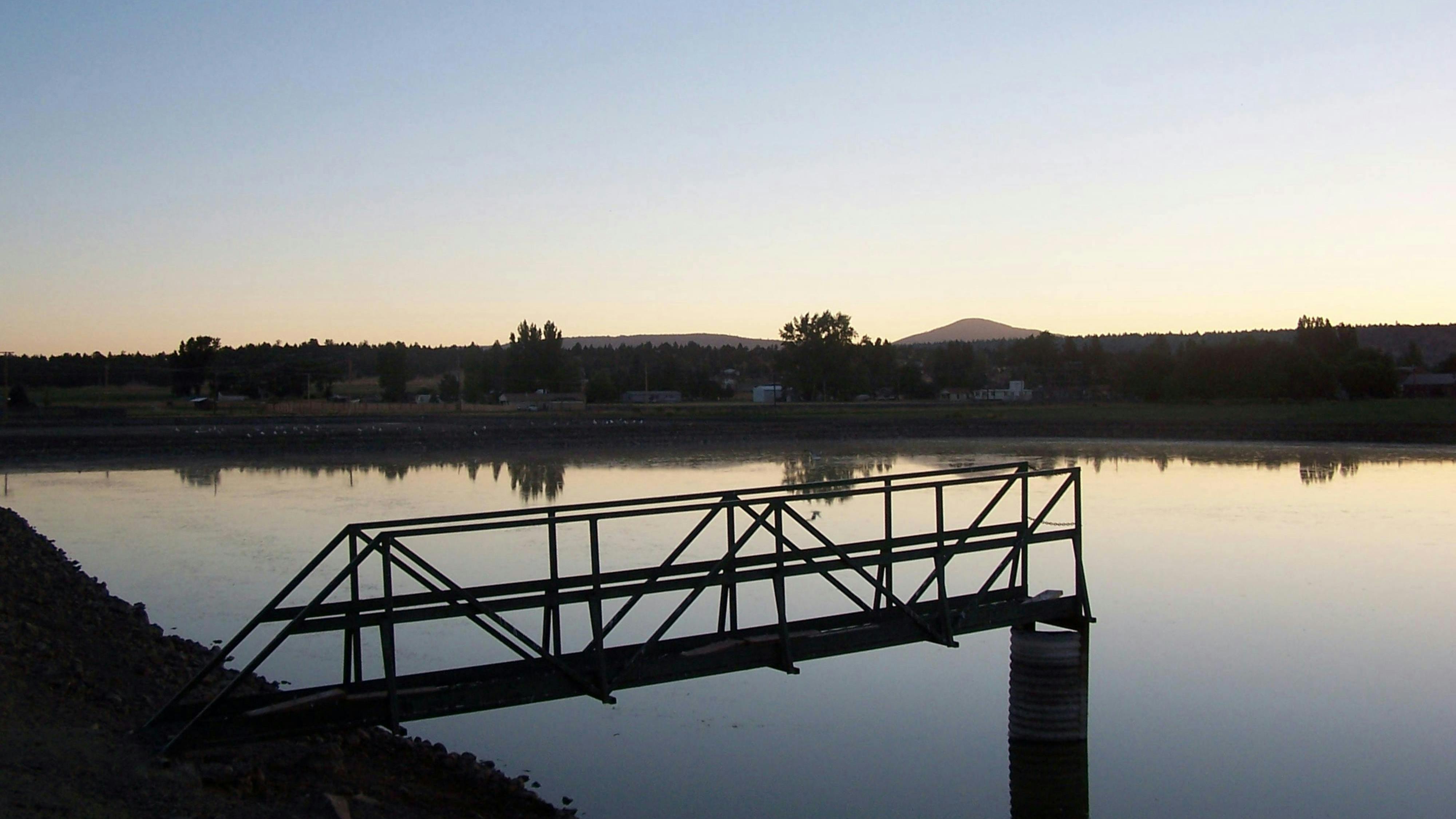 A catwalk over a wastewater treatment lagoon at sunset.